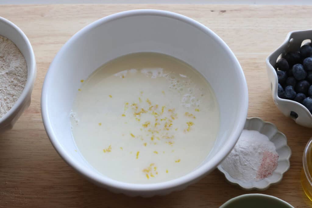 lemon juice and lemon zest and milk in a white bowl to make Freshly Milled Fluffy Lemon Blueberry Pancake Bites