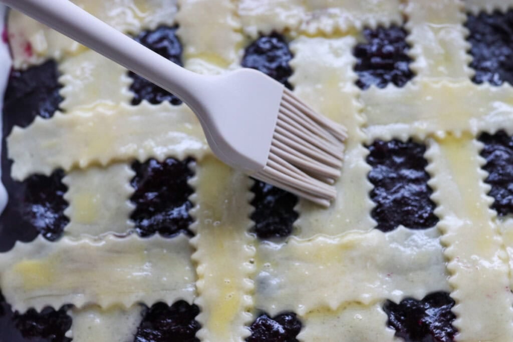 brushing egg wash over top of The Best Blueberry Pie Bars with Fresh Milled Flour