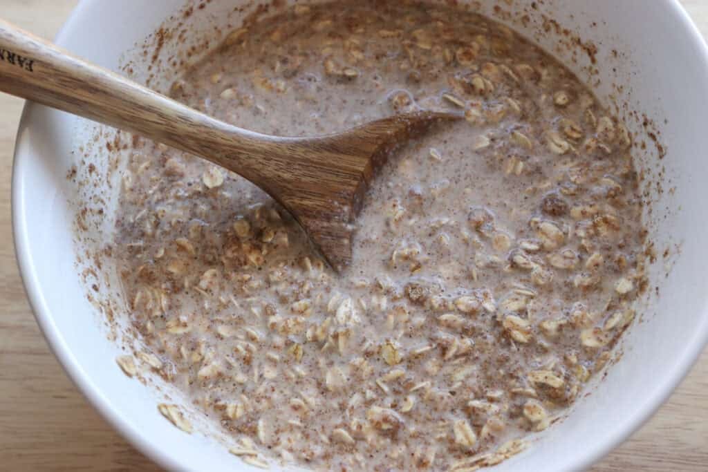 healthy and homemade chai baked oatmeal batter in a white bowl with a wooden spoon