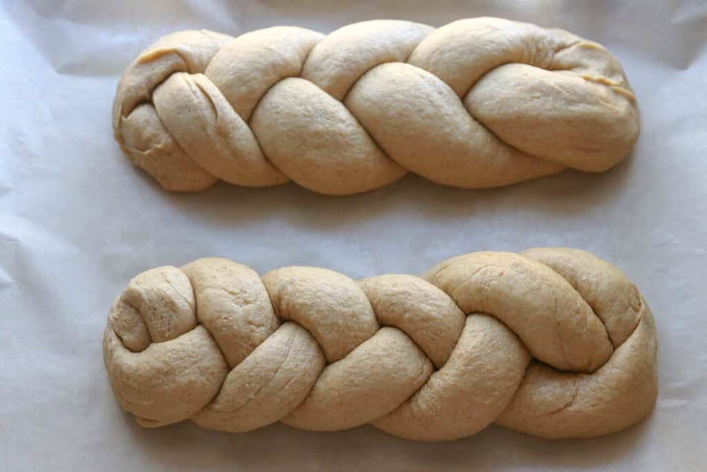 two loaves of freshly milled braided challah bread on a piece of parchment