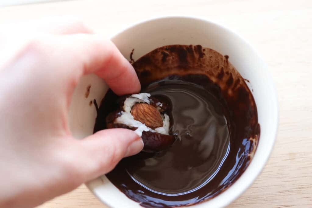 dipping a date in melted chocolate to make Healthy Chocolate Covered Almond Joy Stuffed Dates
