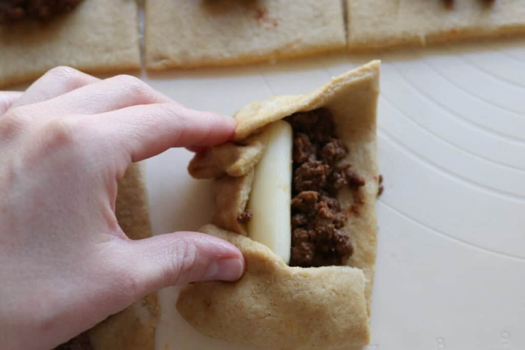 pulling dough up and over a cheese stick to make fresh milled cheesy taco pockets