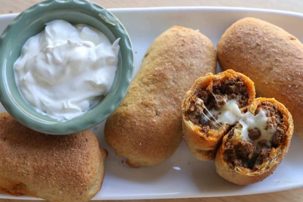 Fresh milled cheesy taco pockets on a white plate with sour cream in a bowl