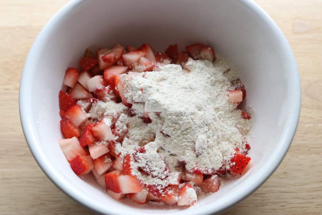 flour on top of diced strawberries in a bowl to make freshly milled glazed strawberry bread