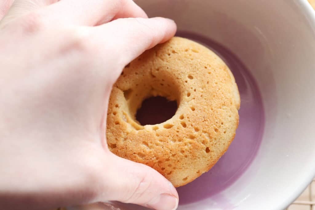 dipping a Homemade Baked Spring Donut with Fresh Milled Flour in a bowl of purple glaze