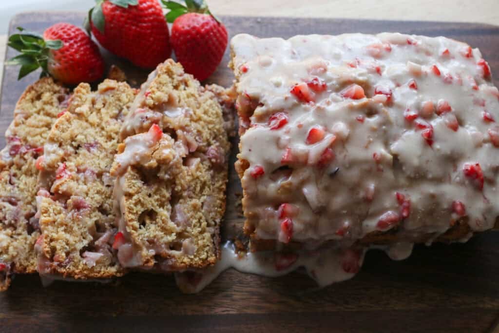 Freshly milled glazed strawberry bread that has been sliced on a board with strawberries