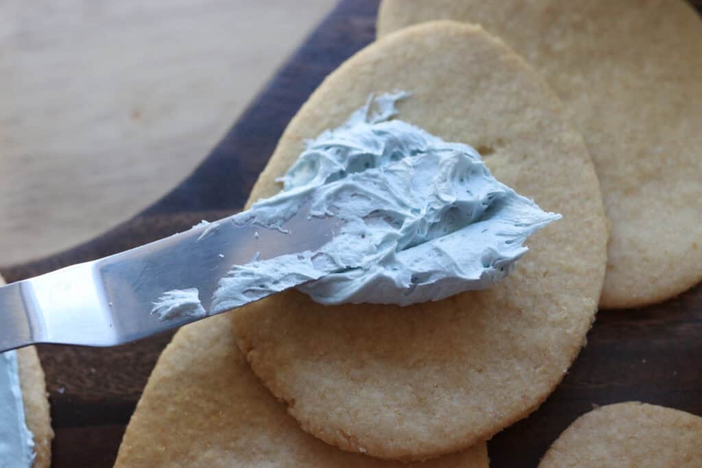 spreading blue frosting on a Fresh milled Easter egg sugar cookie with an offset spatula
