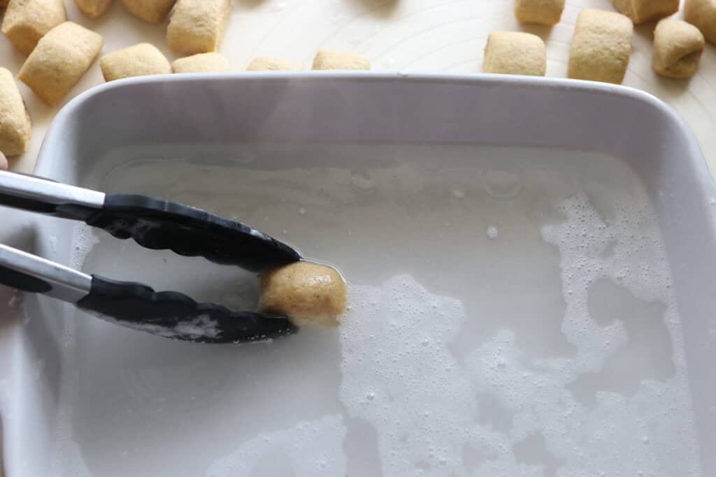 dipping fresh milled soft pretzel bites into a baking soda bath