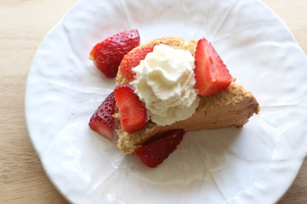 A piece of freshly milled angel food cake on a plate topped with strawberry pieces and whipped cream
