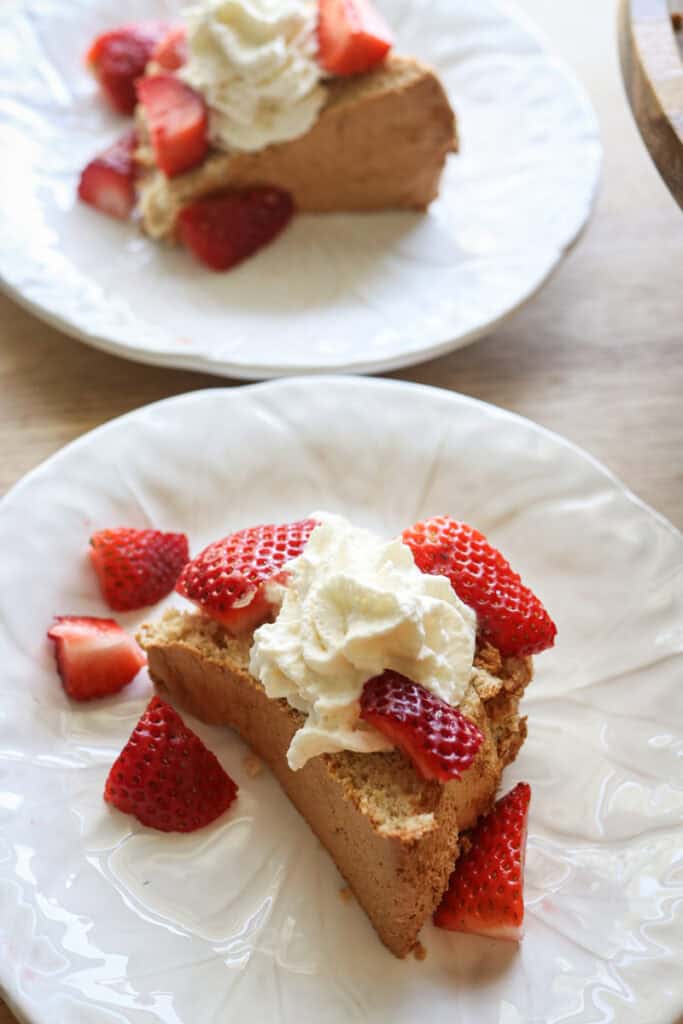 A piece of Freshly milled angel food cake on a white plate topped with cream and berries