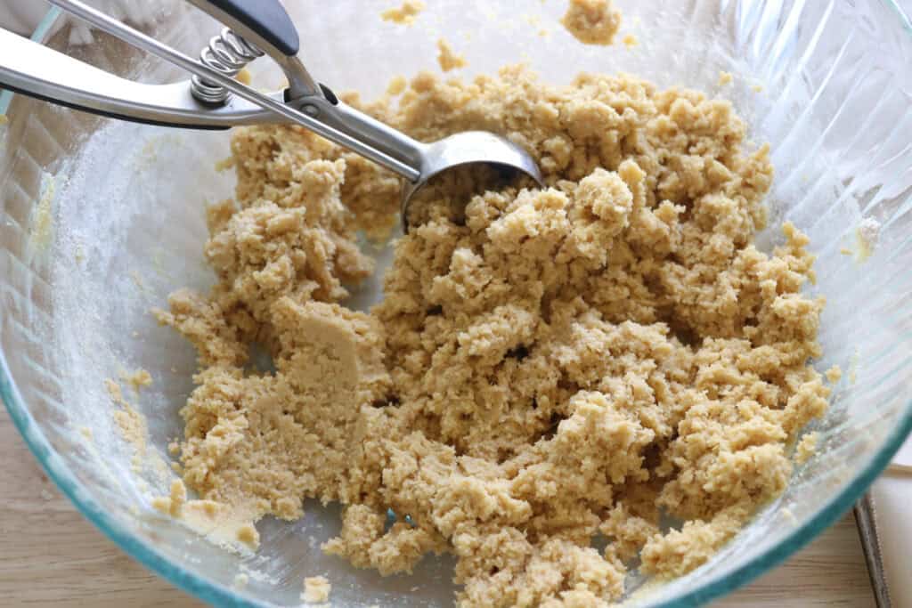 Fresh milled lemon cookie dough in a glass bowl with a cookie scoop