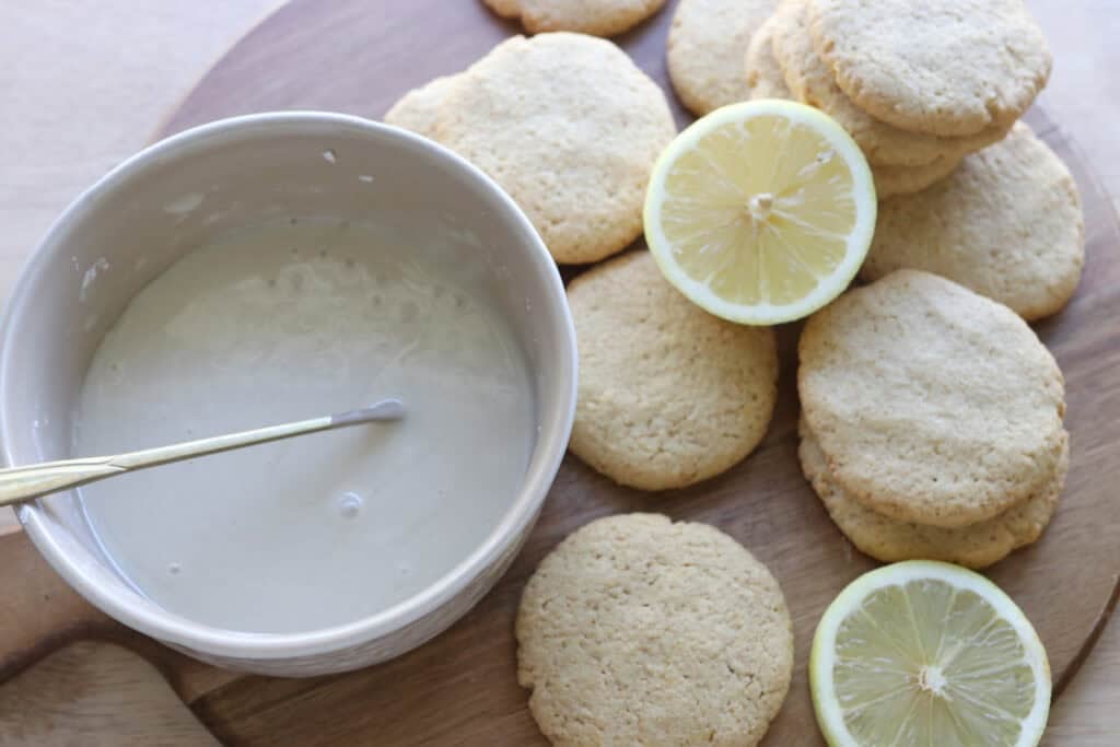 Fresh milled lemon cookies on a wooden board with a bowl of glaze