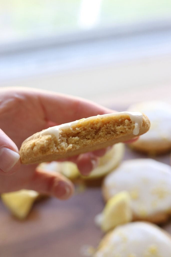 someone holding a Fresh milled glazed lemon cookie with a bite taken out of it