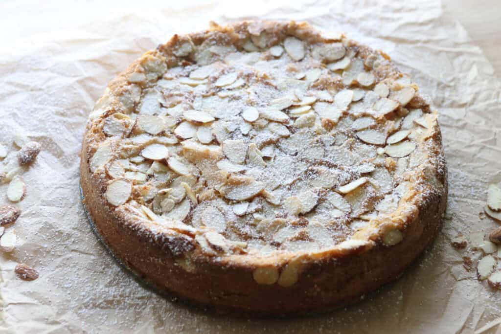 fresh milled almond croissant cake topped with almonds and powdered sugar on parchment paper