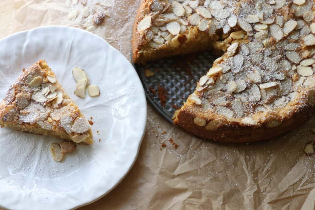 fresh milled almond croissant cake with a slice cut out and on a white plate