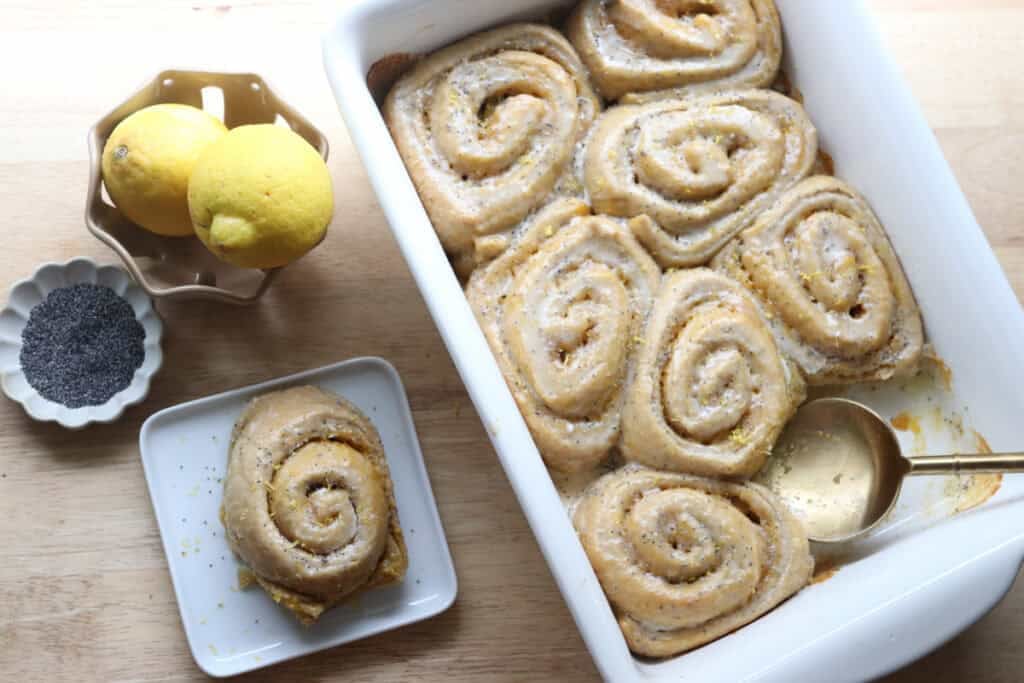 freshly milled lemon poppyseed rolls in a white dish with a plate of poppy seeds and a bowl of lemons