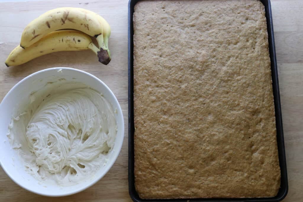 baked freshly milled frosted banana bars with a bowl of cream cheese icing and bananas