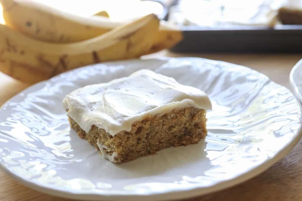 a slice of freshly milled frosted banana bar on a white plate