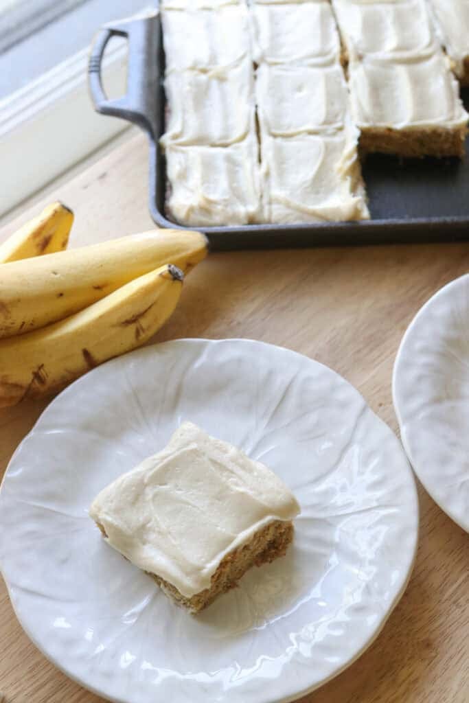 a freshly milled frosted banana bar on a white plate with bananas behind it
