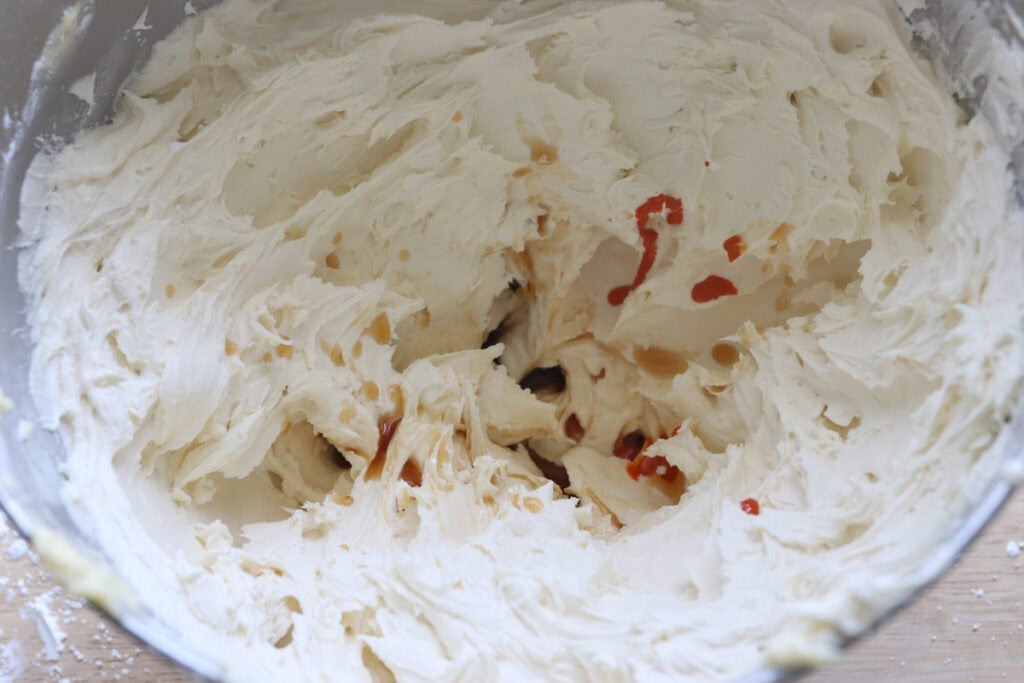 adding orange food coloring to the buttercream for the Freshly milled orange almond poppy seed cake