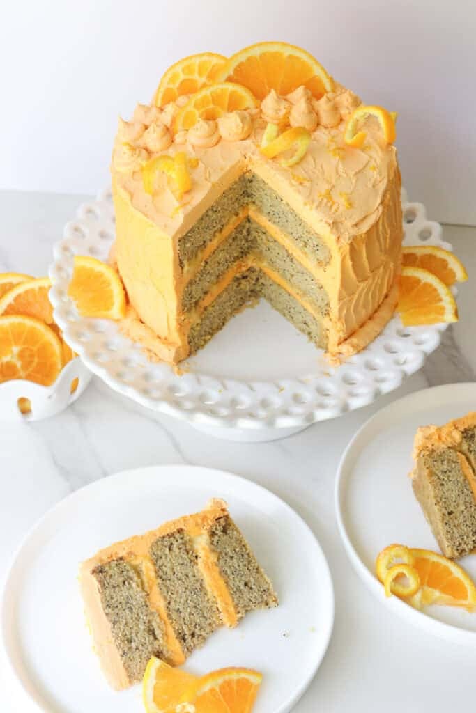 Freshly milled orange almond poppy seed cake with two slices cut out on white plates