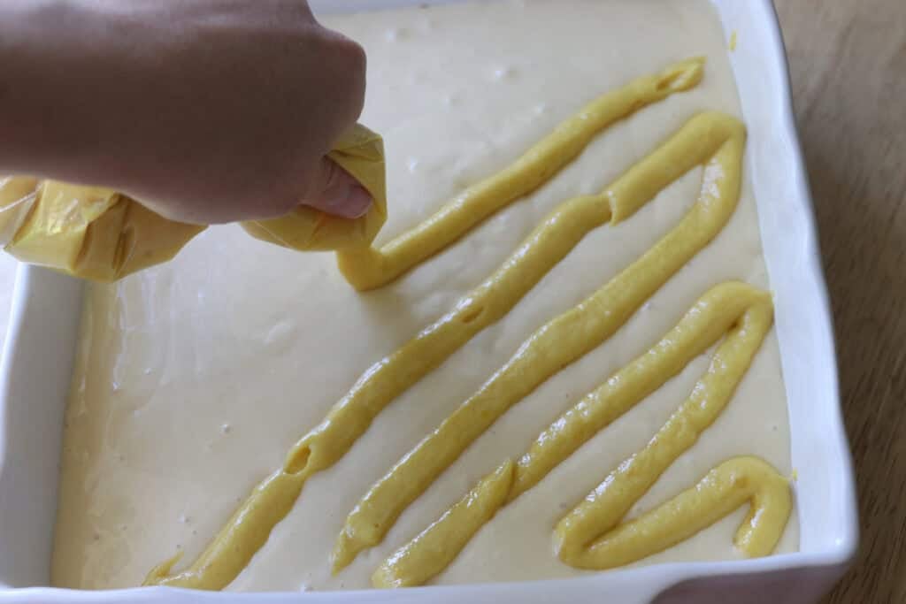squeezing mango puree onto the cheesecake filling to make freshly milled mango cheesecake bars
