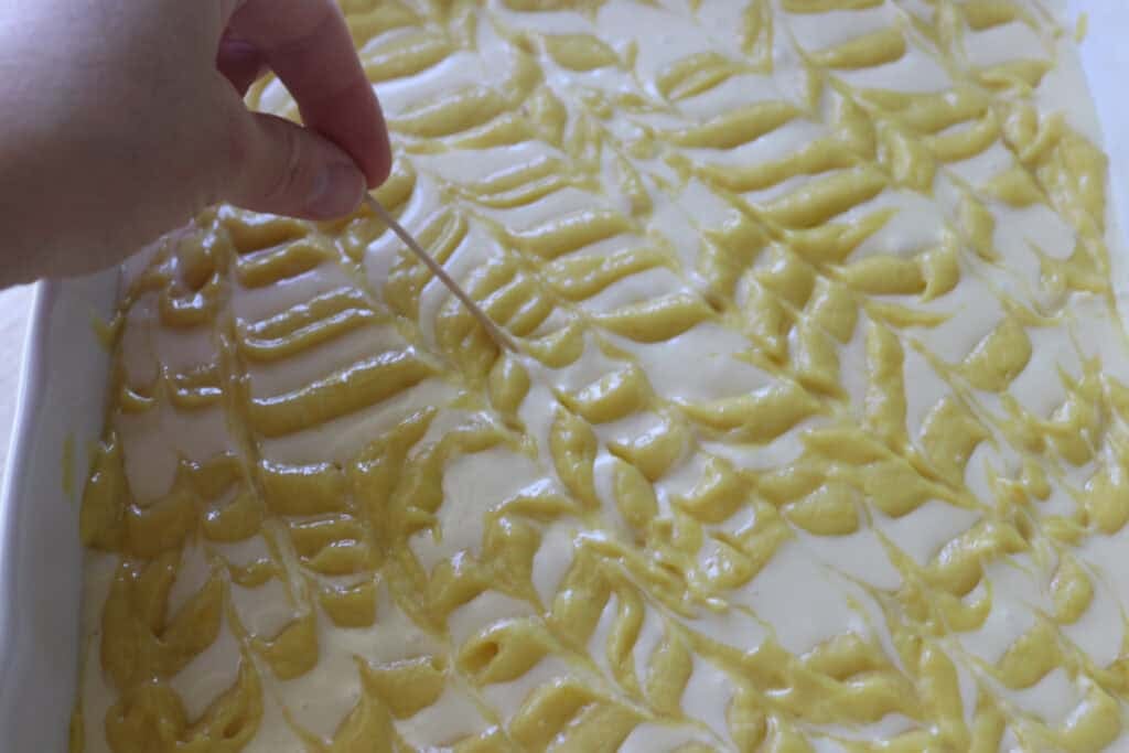 swirling the mango puree into the cheesecake filling to make freshly milled mango cheesecake bars