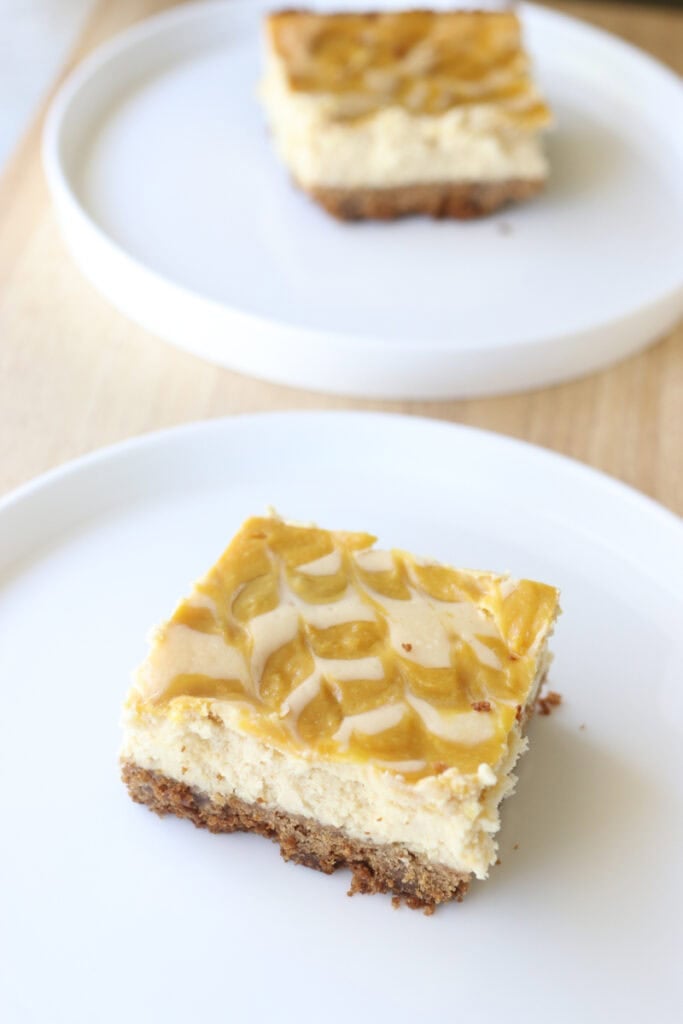 two freshly milled mango cheesecake bars on plates on a wooden board