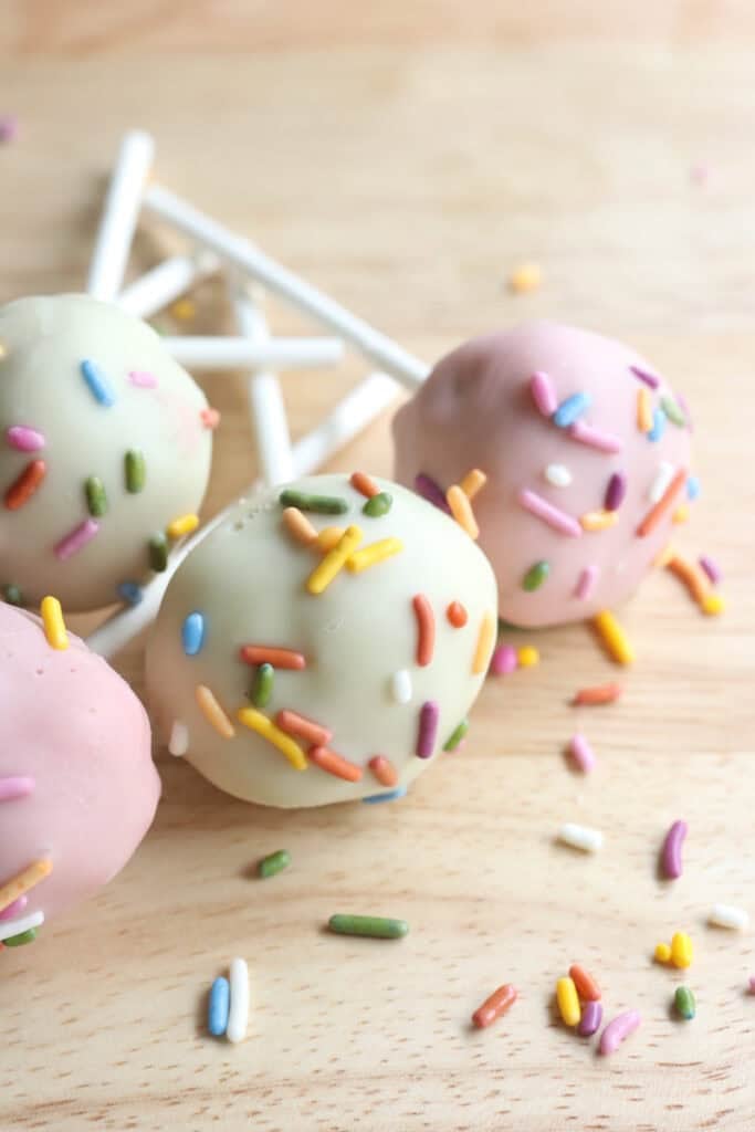 Freshly milled cake pops dipped in chocolate on a board with sprinkles