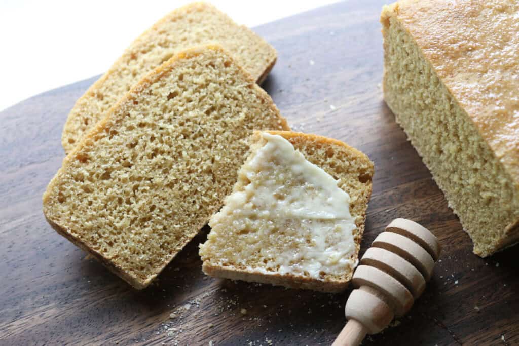 freshly milled english muffin toasting bread with butter on one slice and a honey spoon