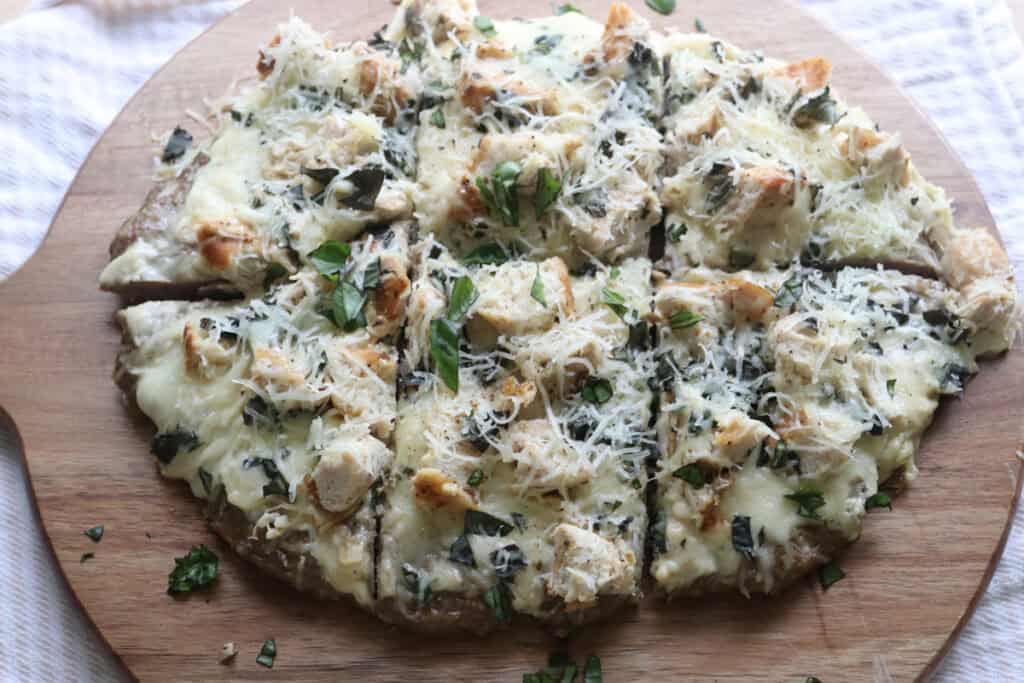 high protein chicken crust chicken alfredo pizza cut into 6 pieces on a board