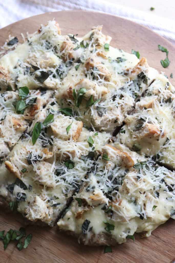 high protein chicken crust chicken alfredo pizza on a wooden board with cheese and fresh herbs