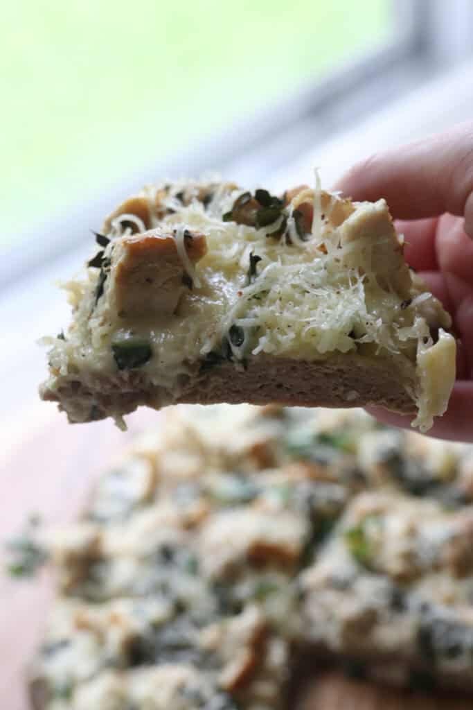 someone holding a slice of high protein chicken crust chicken alfredo pizza