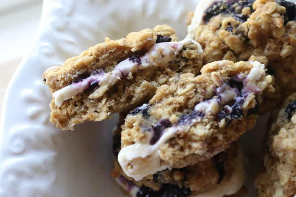 freshly milled blueberry cheesecake oatmeal cream pies on a white plate cut in half